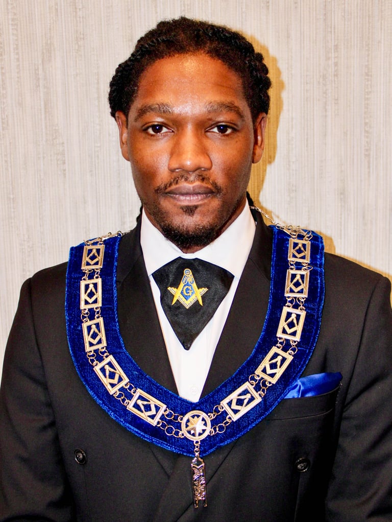 Man in formal black suit wearing blue and gold Masonic ceremonial regalia with emblems and chain