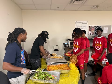 Group of people in casual clothing serving food from trays at an indoor community event or gathering