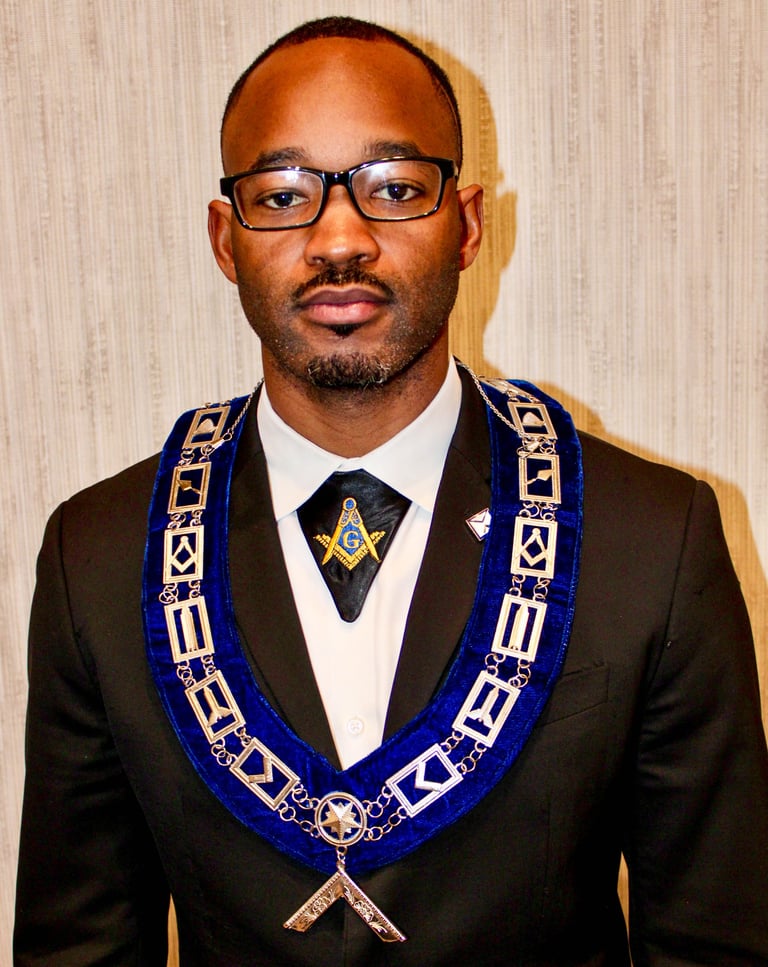 Man wearing black suit and glasses with blue Masonic regalia and emblem against beige background