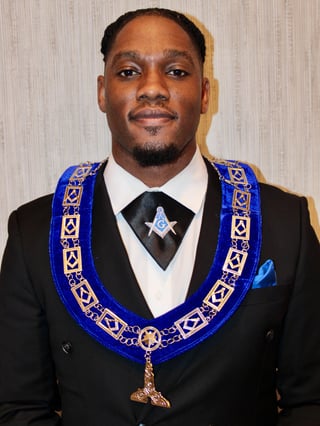 Man in formal black suit wearing blue and gold Masonic regalia with emblem pendant